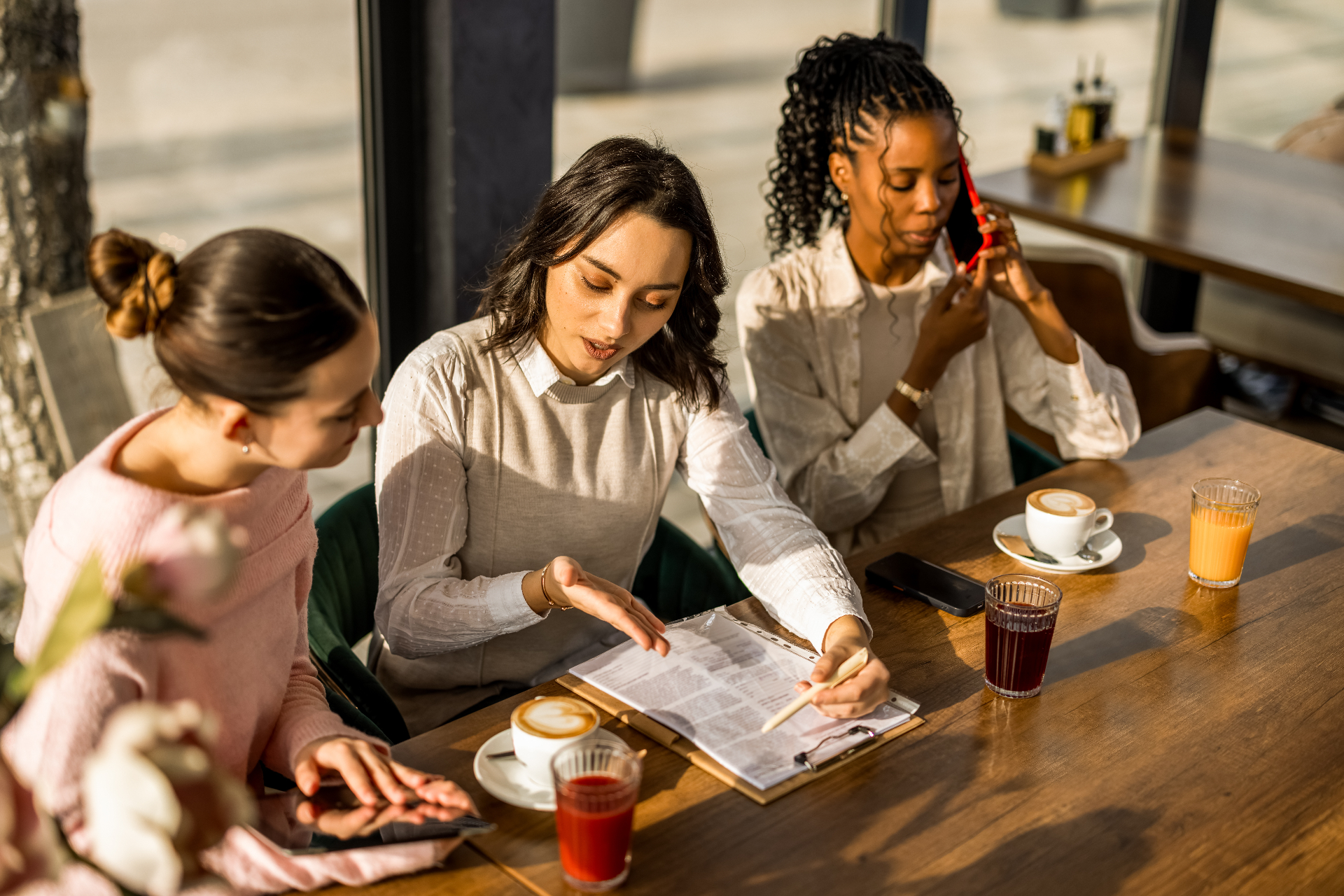 Trois femmes échangeant autour d'une table dans un café lumineux.